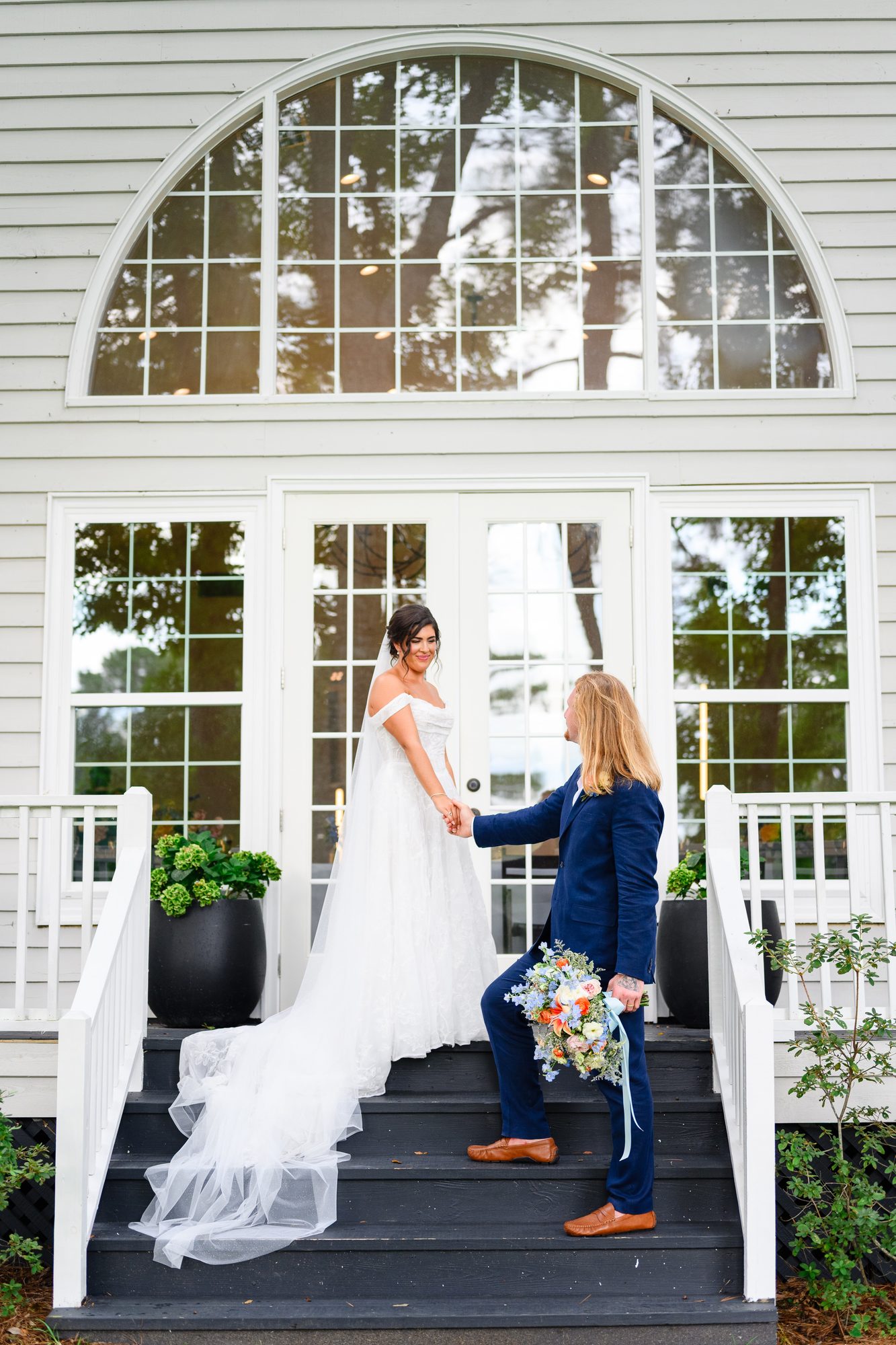 Groom takes the bride's hand on the steps beneath an arched window, Myrtle Beach wedding