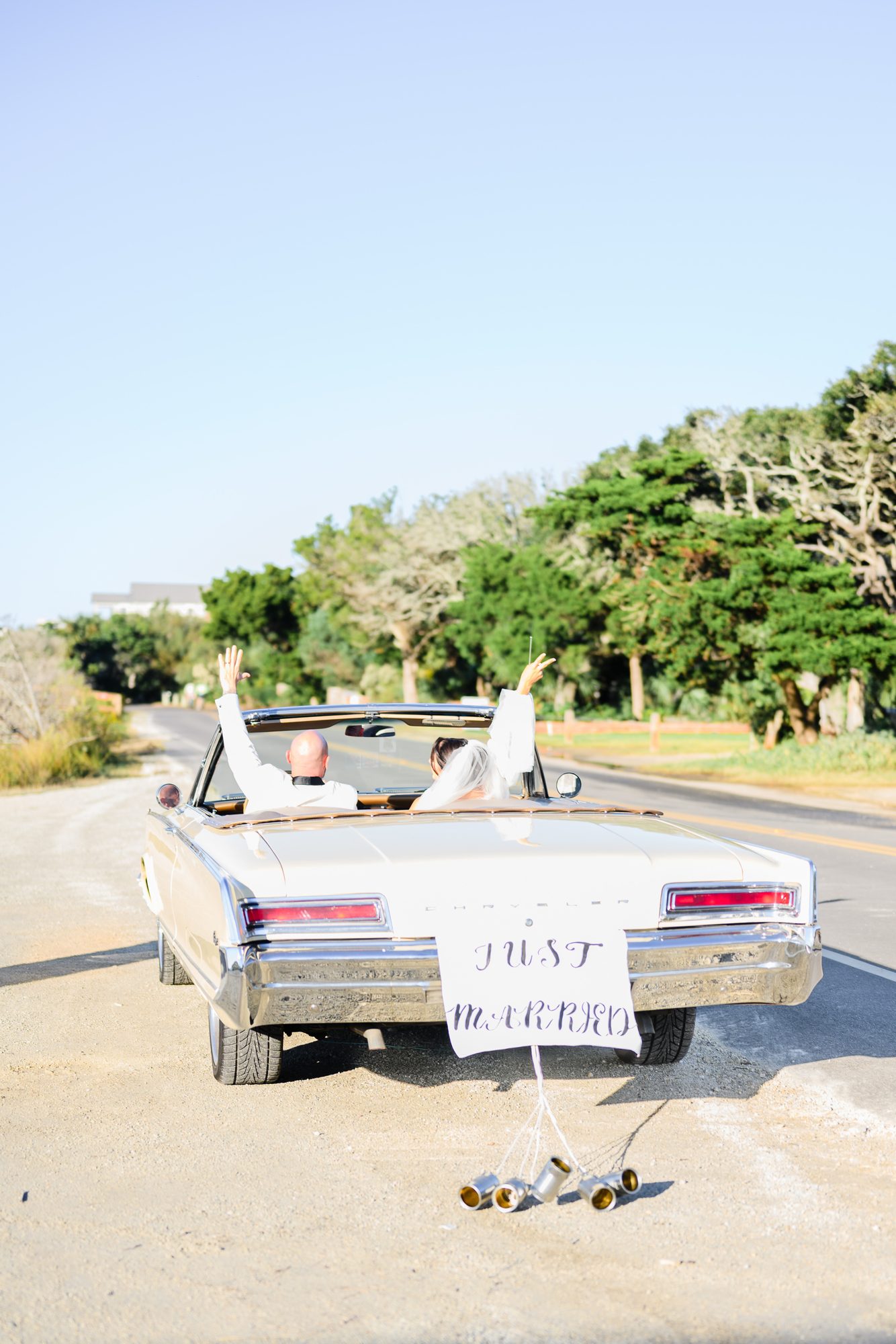 Newlyweds wave from a vintage convertible with a Just Married sign