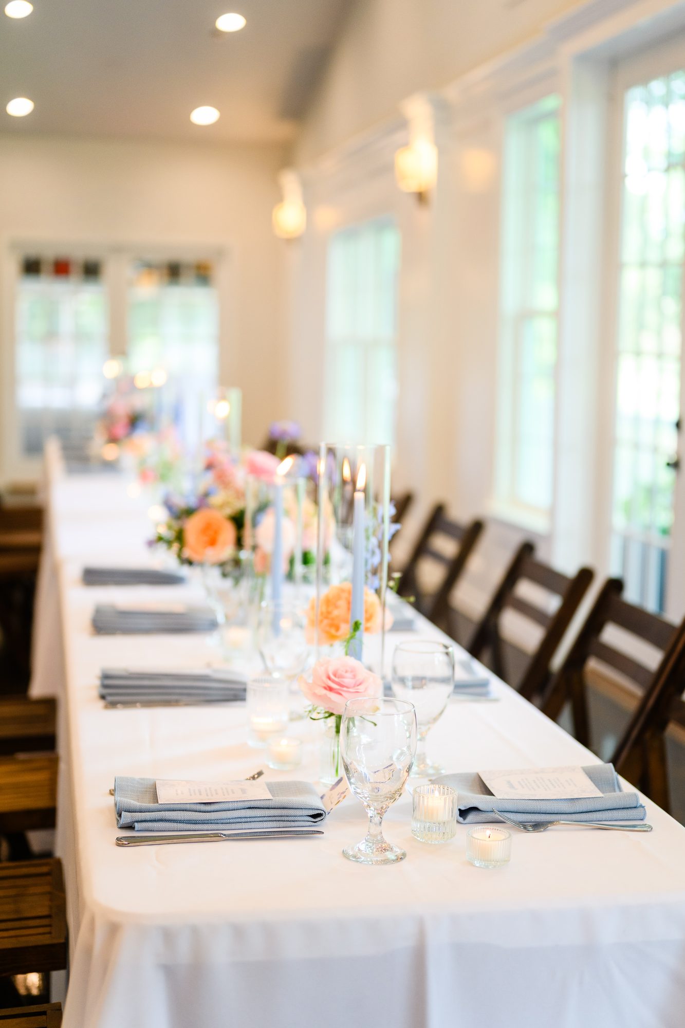 Long reception tables with white linens and colorful florals inside The Village House
