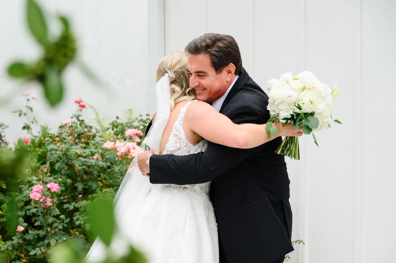 Bride hugs her father among pink roses before the ceremony at White Oaks Farm